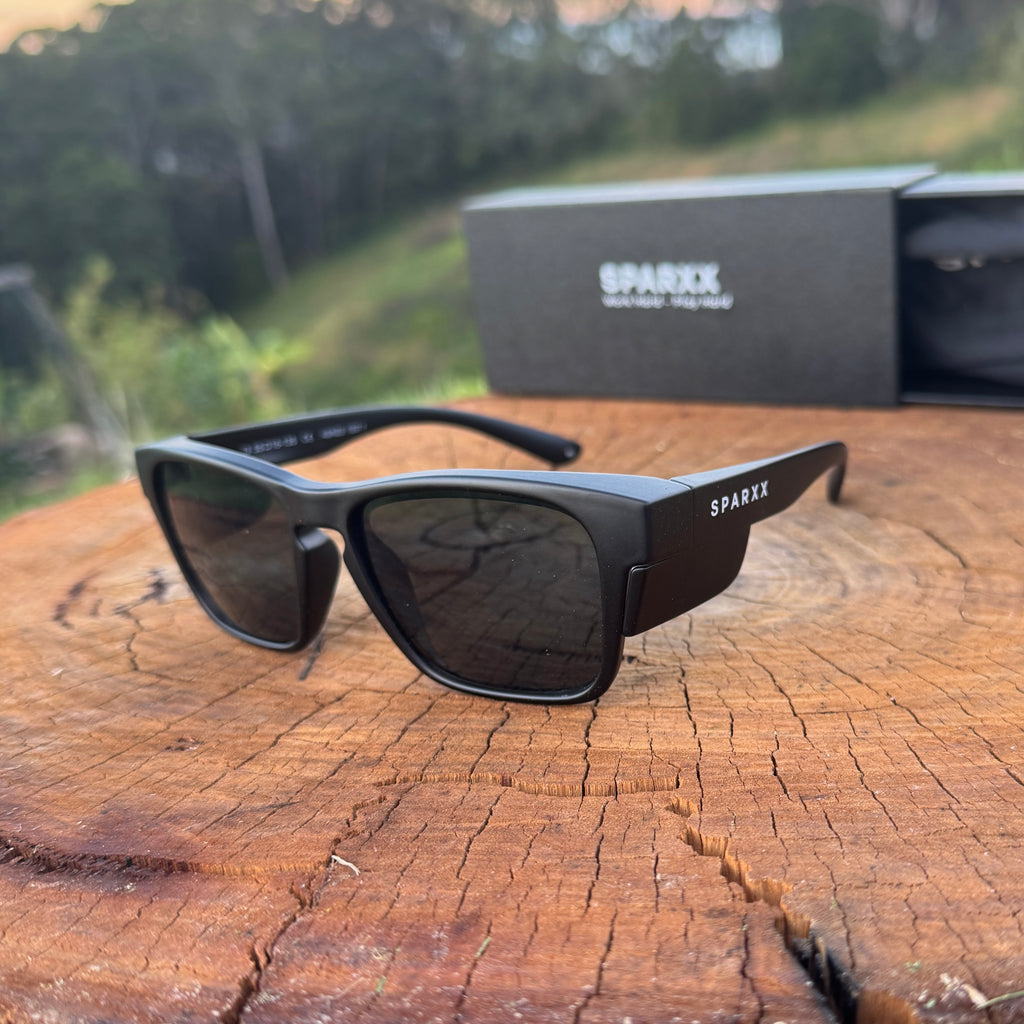 Black sunglasses with 'Sparx' branding on a wooden surface with a blurred natural background