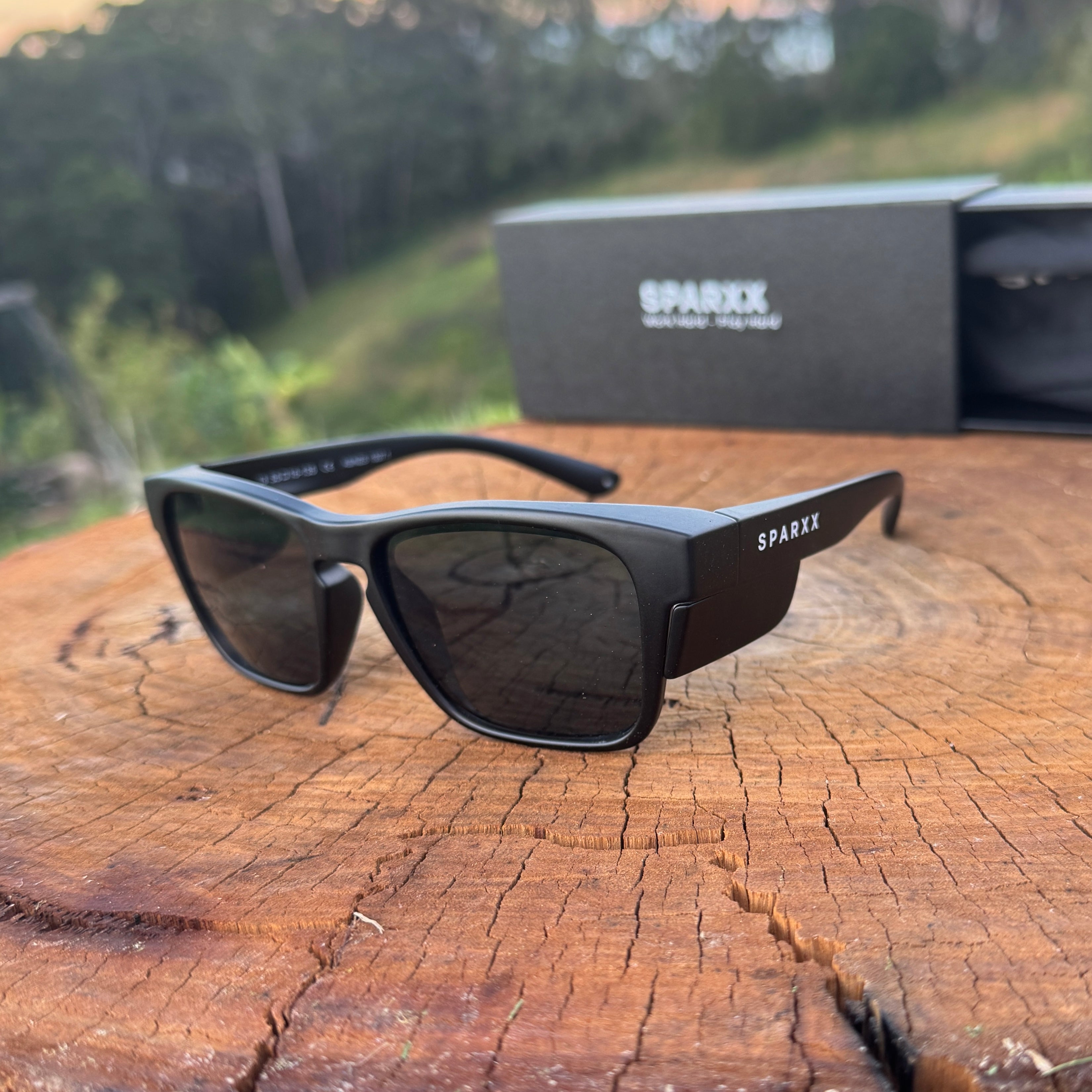 Black sunglasses with 'Sparx' branding on a wooden surface with a blurred natural background